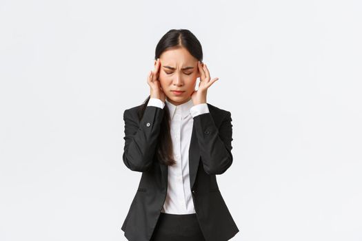 Businesswoman trying to focus, suffering migraine before important business meeting. Asian female entrepreneur touching temples and grimacing from pain, having headache, white background.