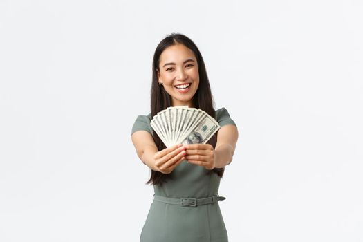 Happy smiling asian female business owner, shop manager showing money she earned at online store, holding cash and rejoicing, show-off with her income, standing white background.
