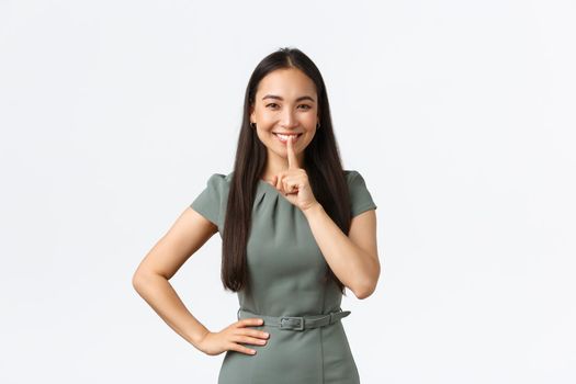 Small business owners, women entrepreneurs concept. Cheerful pretty asian woman having secret, prepare surprise asking keep quiet, show shhh, hush gesture and smiling, white background.