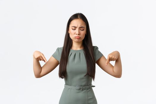 Small business owners, women entrepreneurs concept. Disappointed gloomy asian woman complaining unfair situation, looking with regret and jealousy, pointing fingers down upset.