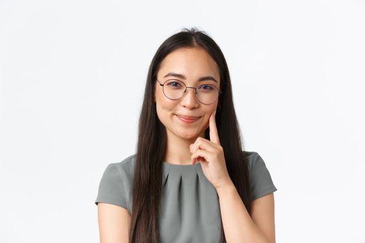 Small business owners, startup and e-commerce concept. Smiling pretty asian woman in glasses grinning and blushing delighted, touching her cheek, promote skincare product, white background.