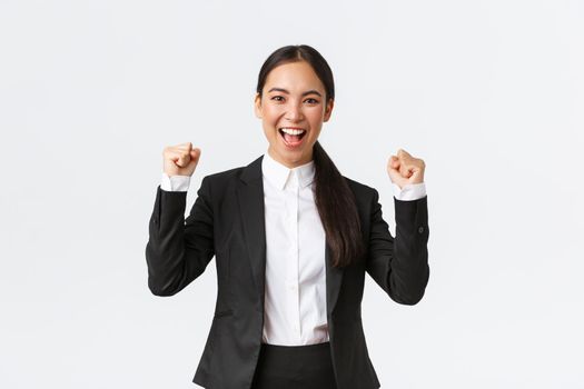 Successful winning female entrepreneur in black suit, fist pump and shouting yes excited, celebrating victory. Businesswoman triumphing over big achievement over white background.