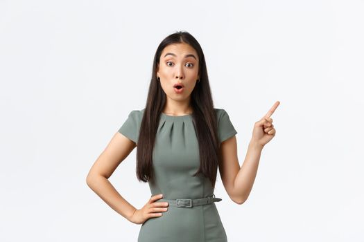 Small business owners, women entrepreneurs concept. Surprised and amazed asian businesswoman asking question about product, pointing finger upper right corner and look astounded.