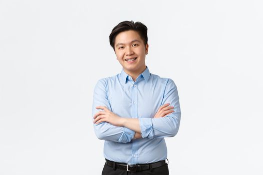 Business, finance and people concept. Professional confident asian businessman with teeth braces, smiling pleased, cross arms chest, standing white background, Salesman showing product.