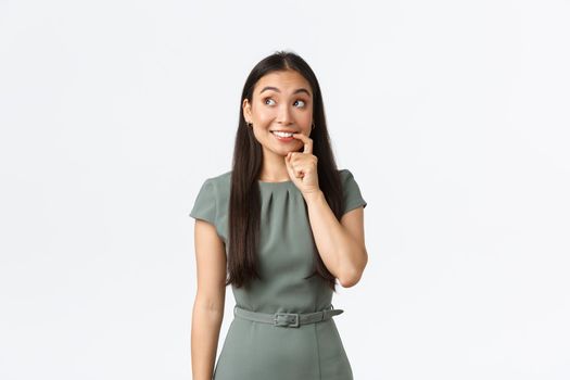 Small business owners, women entrepreneurs concept. Tempting and excited cute asian woman biting finger and looking with desire, thinking, making decision, standing white background.