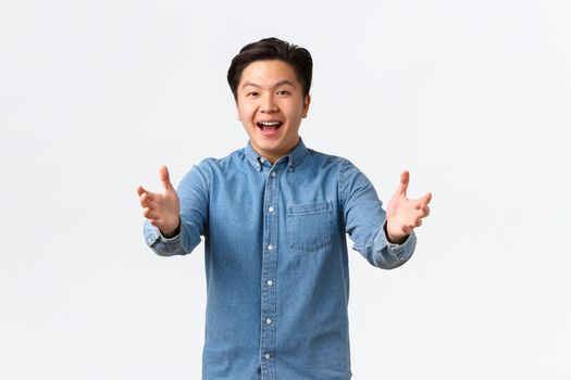 Happy friendly-looking asian male student congratulating friend, reaching hands forward for hug, saying congrats, praising peson with great job, standing white background excited.