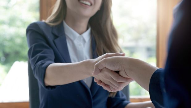 Closeup of unrecognizable happy businesswoman shaking hands with business partner after signing contract during meeting in office..