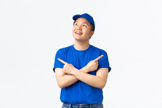 Dreamy smiling asian delivery guy with braces, wearing uniform, dreaming about something, looking upper left corner with pleased grin and pointing sideways, both good variants.