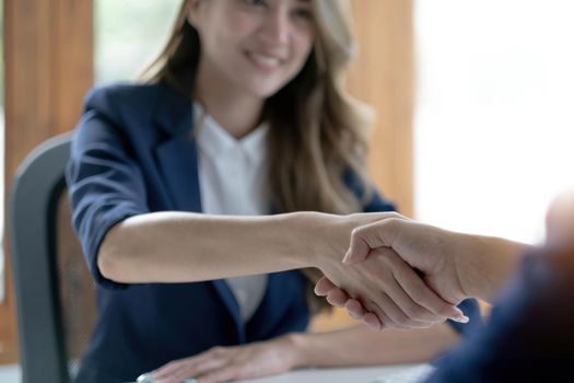 Closeup of unrecognizable happy businesswoman shaking hands with business partner after signing contract during meeting in office..
