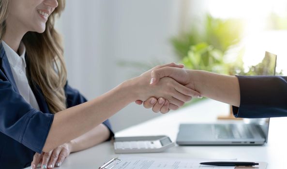 Closeup of unrecognizable happy businesswoman shaking hands with business partner after signing contract during meeting in office..