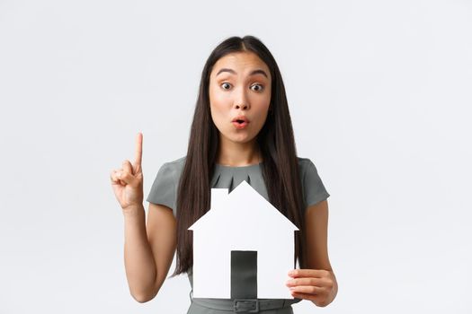 Insurance, loan, real estate and family concept. Thoughtful and creative asian woman have idea, found perfect home or apartment, raise index finger in eureka sign, holding paper house.