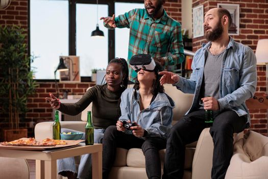 Multiethnic group of people playing video games with vr glasses, using augmented reality and 3d simulation to play competition. Cheerful friends enjoying headset and game at house party.