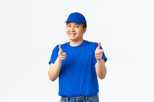 Cheerful friendly, smiling asian delivery guy in blue cap and t-shirt pointing fingers at camera, compliment nice choice, guarantee and ensure you in company services, praising nice job.