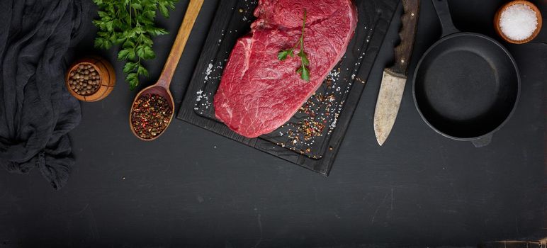 Raw beef tenderloin lies on a brown wooden board, black table. View from above