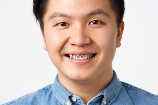 Orthodontics and stomatology concept. Headshot of happy asian man smiling, showing dental braces, recommend clinic, satisfied with good results, standing white background pleased.