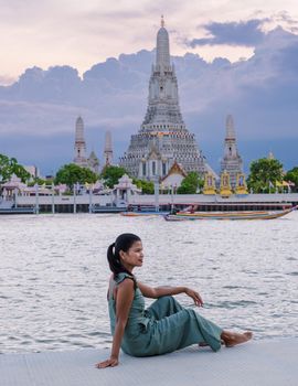 Wat Arun temple Bangkok Thailand, Temple of Dawn, Buddhist temple alongside Chao Phraya River.Beautiful Wat Arun at dusk evening sunset, Asian woman watching sunset alongside Chao Phraya River