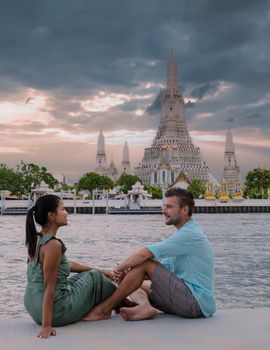 Wat Arun temple Bangkok Thailand, Temple of Dawn, Buddhist temple alongside Chao Phraya River.Beautiful Wat Arun at dusk evening sunset, couple Asian woman and European men watching sunset