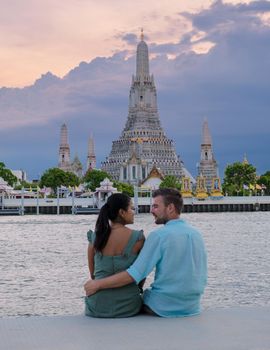 Wat Arun temple Bangkok Thailand, Temple of Dawn, Buddhist temple alongside Chao Phraya River.Beautiful Wat Arun at dusk evening sunset, couple Asian woman and European men watching sunset