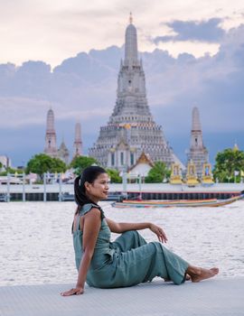 Wat Arun temple Bangkok Thailand, Temple of Dawn, Buddhist temple alongside Chao Phraya River.Beautiful Wat Arun at dusk evening sunset, Asian woman watching sunset alongside Chao Phraya River