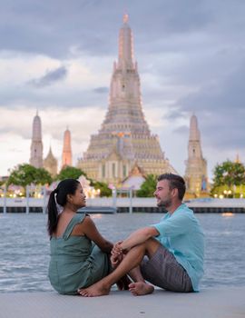 Wat Arun temple Bangkok Thailand, Temple of Dawn, Buddhist temple alongside Chao Phraya River.Beautiful Wat Arun at dusk evening sunset, couple Asian woman and European men watching sunset