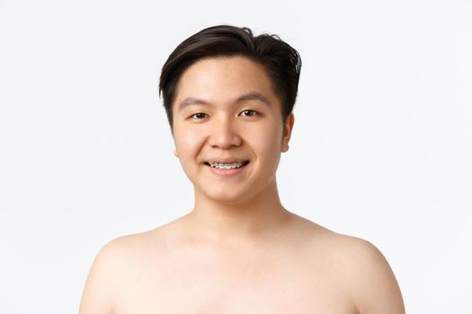 Beauty, skincare and hygiene concept. Close-up of smiling asian guy with braces standing naked over white background, advertisement of dermatology products, cleansers for acne prone skin.