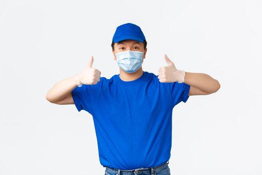Contactless delivery, covid-19 shipping, preventing virus concept. Smiling confident asian courier in medical mask and gloves showing thumbs-up guarantee safe shipment during coronavirus.