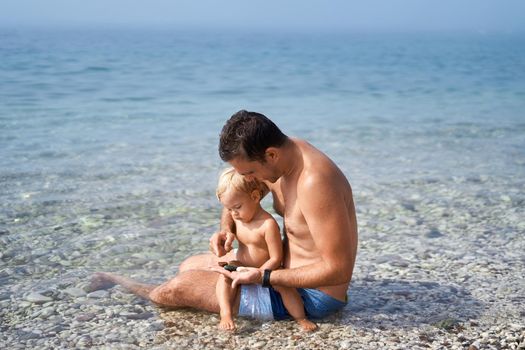 Dad and a little girl are sitting and sorting out sea pebbles. High quality photo