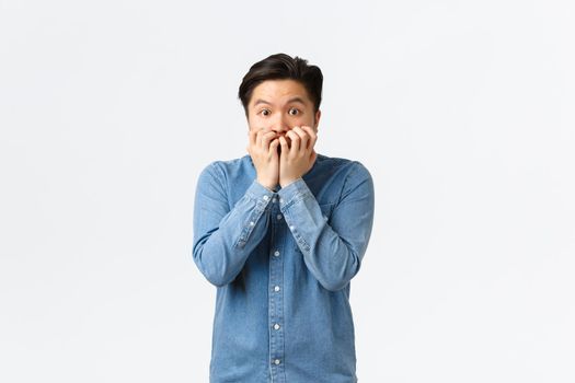 Scared asian guy shivering from fear and biting fingersnails, looking afraid and insecure at camera. Frightened man in panic stare anxious, witness terrible accident, watching horror movie.