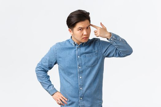 Serious angry asian man looking with dismay at employee, scolding person making stupid mistake, tap temple with finger and stare frustrated, standing white background upset.