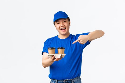Online orders, takeaway and employees concept. Friendly cheerful male courier in blue uniform ensure fast delivery from restaurants or cafes, pointing finger at coffee and smiling, white background.