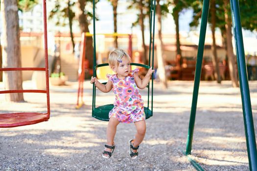 Little girl sits on a swing and looks away. High quality photo