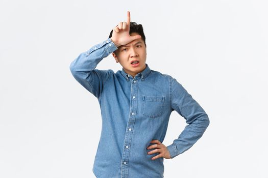 Disappointed angry asian man, coach scolding team for losing, showing loser gesture with displeased upset face, complaining, feeling uneasy and distressed, standing white background.