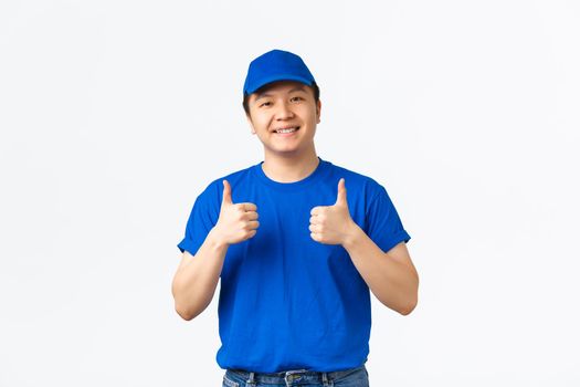 Friendly cheerful asian courier in blue uniform, smiling with braces, showing thumbs-up, guarantee, provide best offers, fast delivery and cheap prices, recommend shipping company.