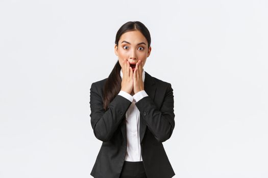 Shocked concerned asian businesswoman facing troublesome situation, drop jaw and stare startled at camera, dont know what do, feeling panic and shook, standing white background.