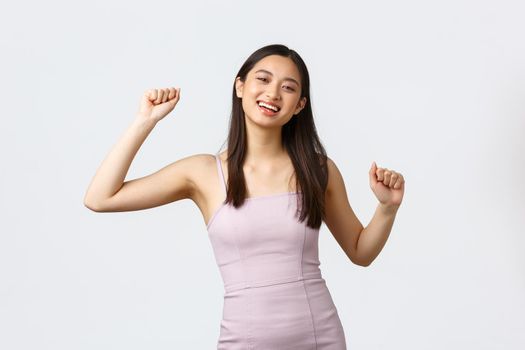 Luxury women, party and holidays concept. Happy excited smiling asian woman do winner dance, become champion, celebrating success, wearing evening dress, rejoicing over good news.