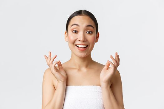 Beauty, cosmetology and spa salon concept. Surprised and happy beautiful asian girl in towel react to clean perfect skin after skincare or massage therapy, look impressed and satisfied.