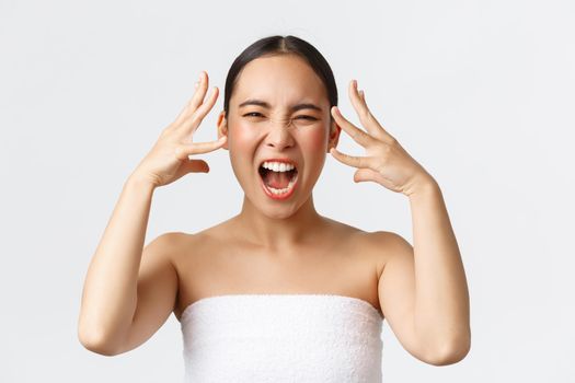 Beauty, cosmetology and spa salon concept. Close-up of outraged, mad distressed asian woman in bath towel screaming and shaking hands near head, feeling furious after bad service in beauty clinic.