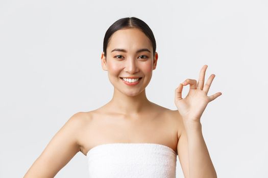 Beauty, cosmetology and spa salon concept. Close-up of beautiful asian female in towel showing okay gesture, satisfied with excellent service in beauty clinic, pleased with results, smiling delighted.
