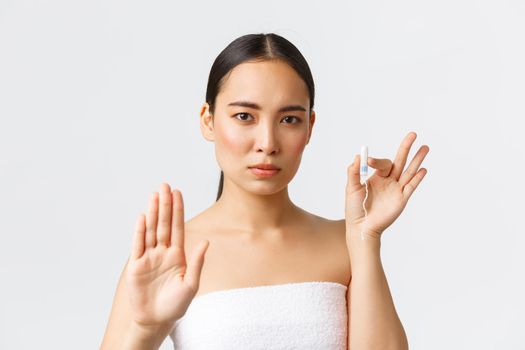 Beauty, personal and intimate care menstrual hygiene concept. Serious-looking beautiful asian girl in towel, showing stop gesture and tampon, encourage use menstrual cups or organic products.