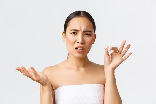 Beauty, personal and intimate care menstrual hygiene concept. Close-up of confused asian girl in bath towel arguing about tampons, looking displeased, standing white background complaining.