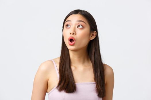 Beauty, fashion and people emotions concept. Impressed and amazed beautiful asian girl drop jaw, gasping and saying wow speechless, looking upper left corner excited, white background.