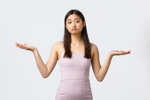 Luxury women, party and holidays concept. Clueless gloomy asian girl in evening dress, shrugging with hands spread sideways, dont know what product better, smirk unaware and doubtful.
