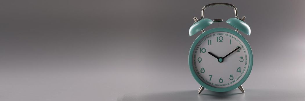 Turquoise alarm clock at ten o'clock on gray background. Time control concept