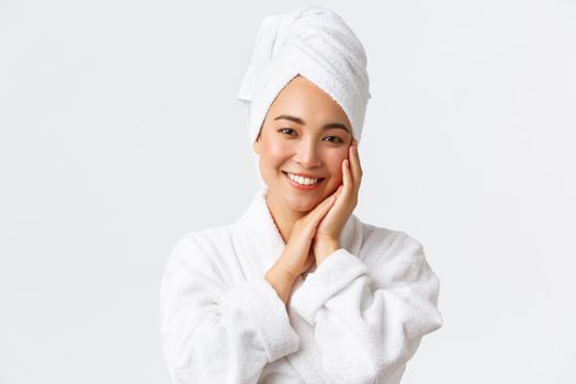 Personal care, women beauty, bath and shower concept. Close-up of beautiful happy asian woman in towel and bathrobe touching face gently, smiling white teeth, promo of skin care and hygiene products.