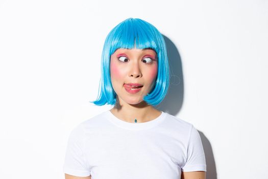 Close-up of funny and silly asian girl entertainer celebrating halloween, wearing blue wig and squinting, showing grimaces.