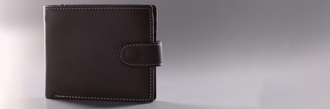 Brown leather closed wallet on gray background. Choosing fashionable wallet concept