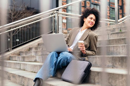 happy young woman relaxed in the city with a coffee and working with her laptop computer, concept of business and urban lifestyle, copy space for text