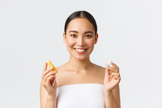 Beauty, personal and intimate care menstrual hygiene concept. Close-up of attractive asian girl in towel showing tampon with and without applicator, smiling at camera, white background.