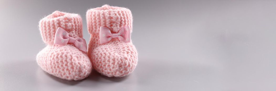 Pink knitted slippers for newborn on gray background. Baby feet in shape of woman feet
