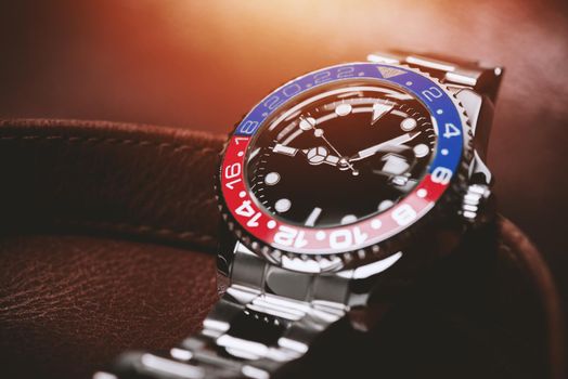 closeup luxury wristwatch for men with black dial blue-red bezel and stainless steel bracelet.